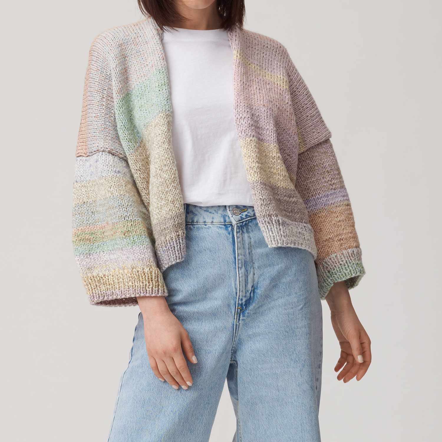 Strickanleitung Jacke aus Creative Chic-Unique: Frau trägt pastellfarbene Strickjacke über weißem T-Shirt und blauen Jeans.