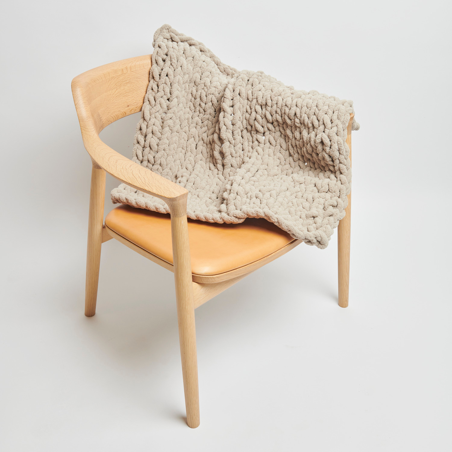 Chenillove Super Big: Weiche, naturfarbene Strickdecke von Rico Design auf einem Holzstuhl drapiert.