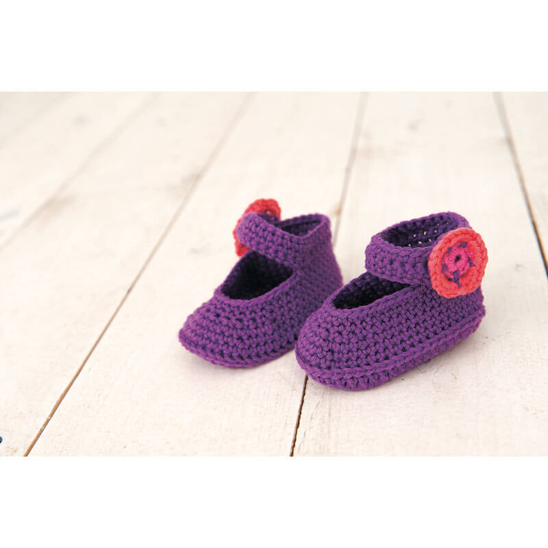 Rico Baby Heft Nr.9: Lila gehäkelte Babyschuhe mit roter Blume auf hellem Holzboden von Rico Design.