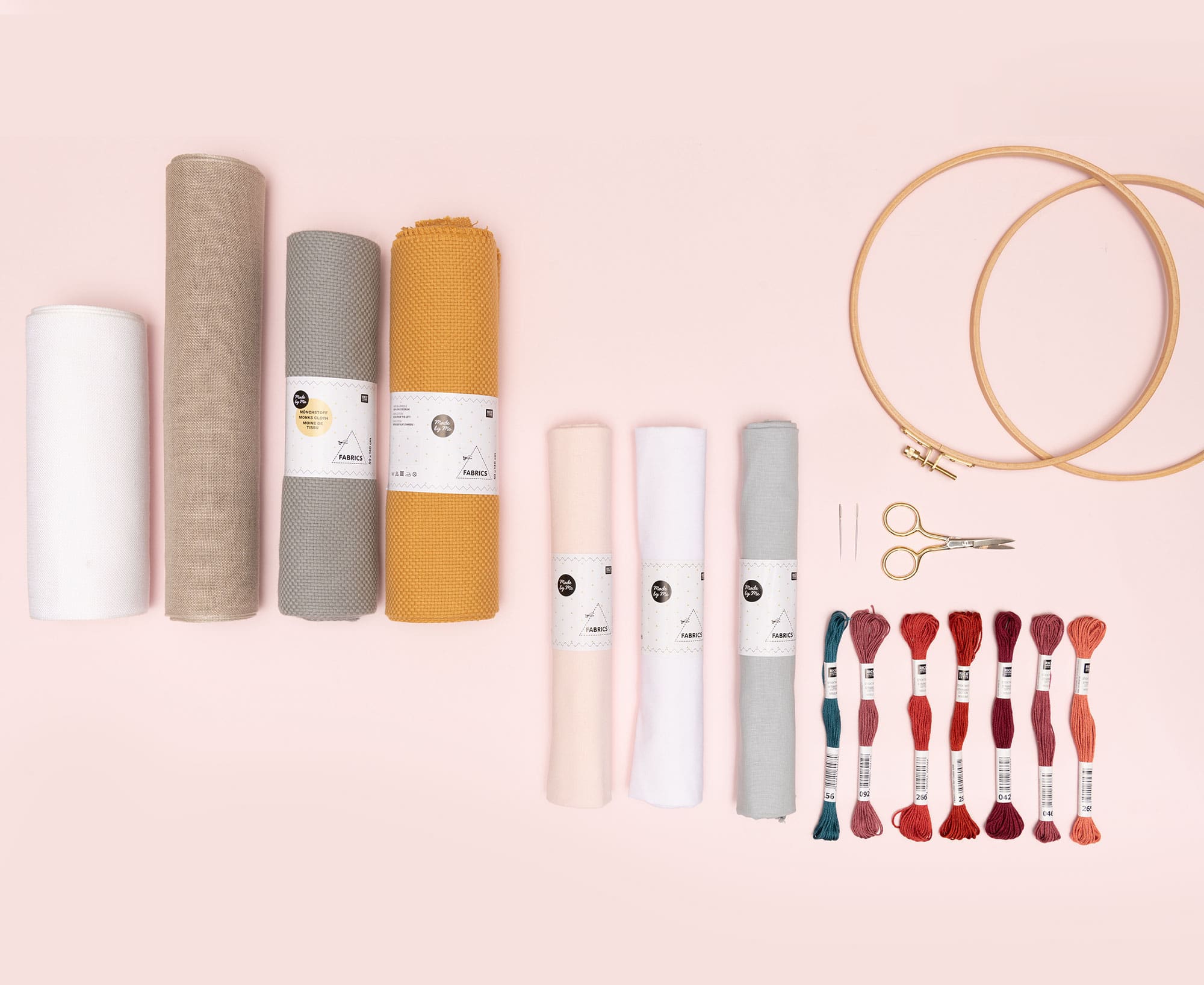 Stickring, Stickgarn, Stoff und Stickzubehör liegen auf rosa Untergrund