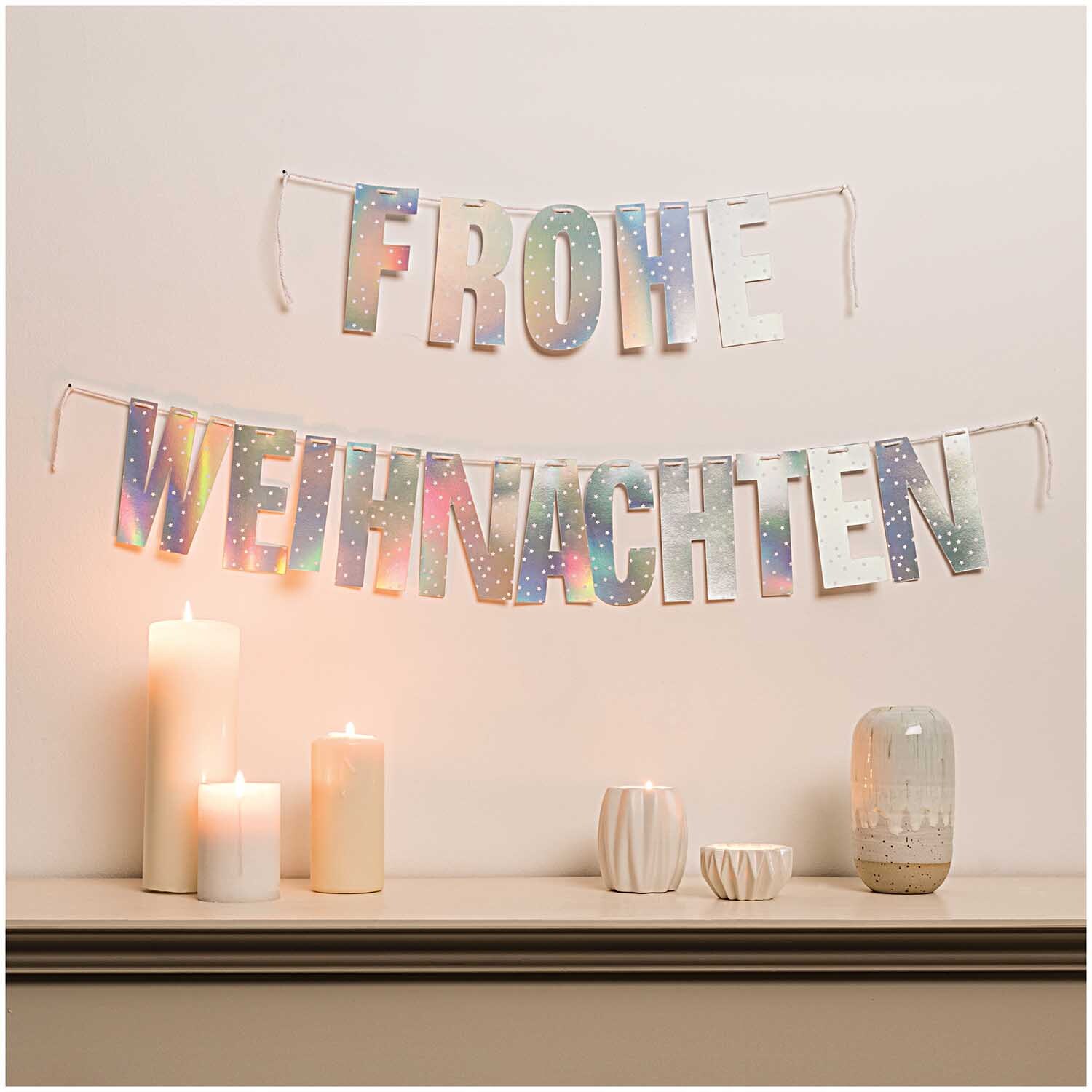 Paper Poetry Girlande Frohe Weihnachten 3m Hot Foil, silber irisierend, dekoriert eine Wand über Kerzen.