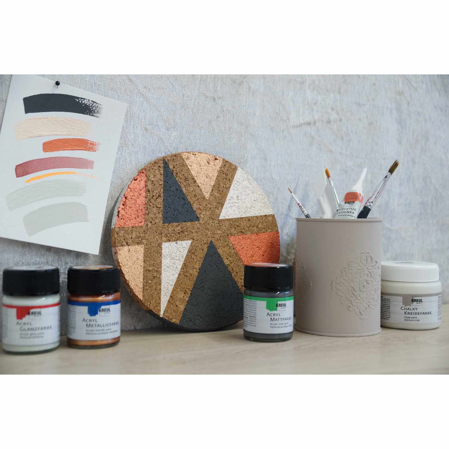 Acryl Metallicfarbe 20ml von KREUL in verschiedenen Farben, neben Pinseln und Farbproben auf einem Tisch arrangiert.