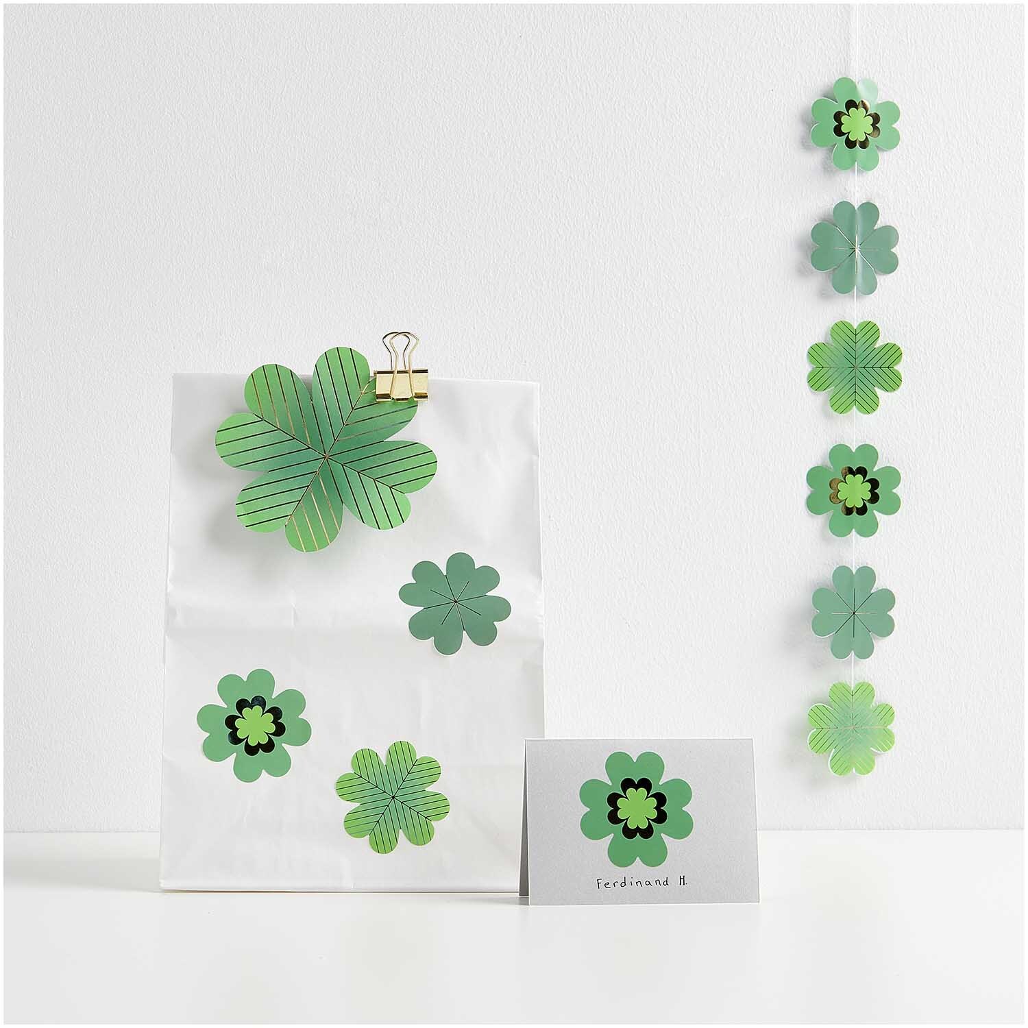 Paper Poetry Sticker Glücksklee auf einer Rolle, dekoriert auf einer weißen Tüte und Karte. Ideal für kreative Bastelprojekte.