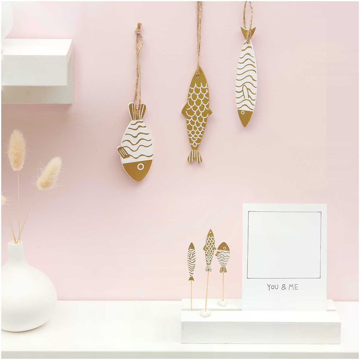 Deko-Picker Fisch Mix gold-weiß 7,5-8,5cm 6 Stück: Elegante Fisch-Dekorationen in Gold und Weiß an rosa Wand. Ideal für stilvolle Raumgestaltung.