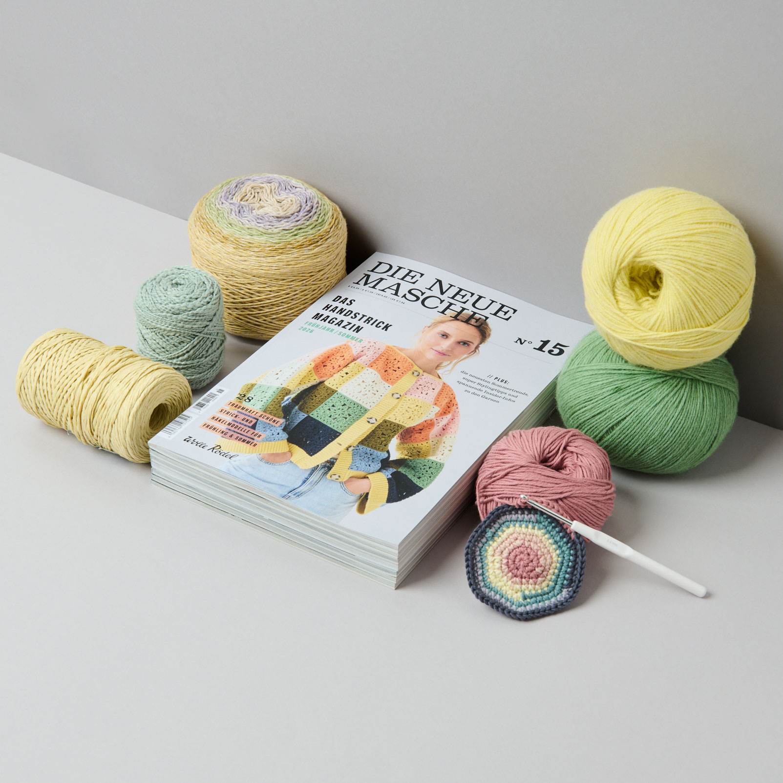 Stapel von Handstrickmagazinen daneben Garne und ein Strickstück mit Stricknadeln. Fotosetting graue Ecke.