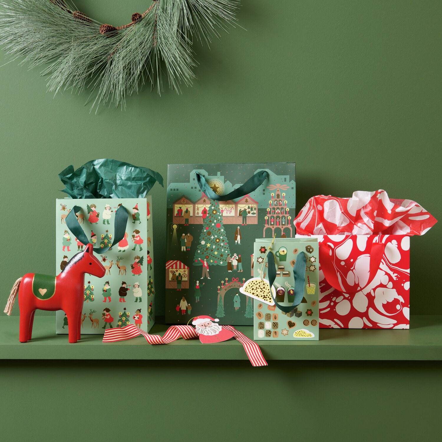 Geschenktüte Marmor Rot/Weiß S auf grünem Hintergrund mit Weihnachtsmotiven und Holzpferd.