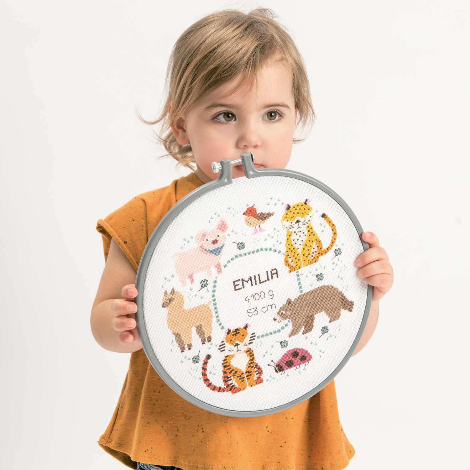 Stickring aus Kunststoff: Kind hält einen grauen Stickring mit Tierstickerei von Rico Design.