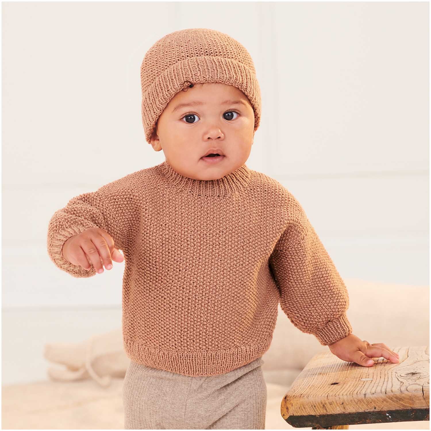 Baby Merino: Ein Baby trägt einen gestrickten Pullover und Mütze in Puder von Rico Design.