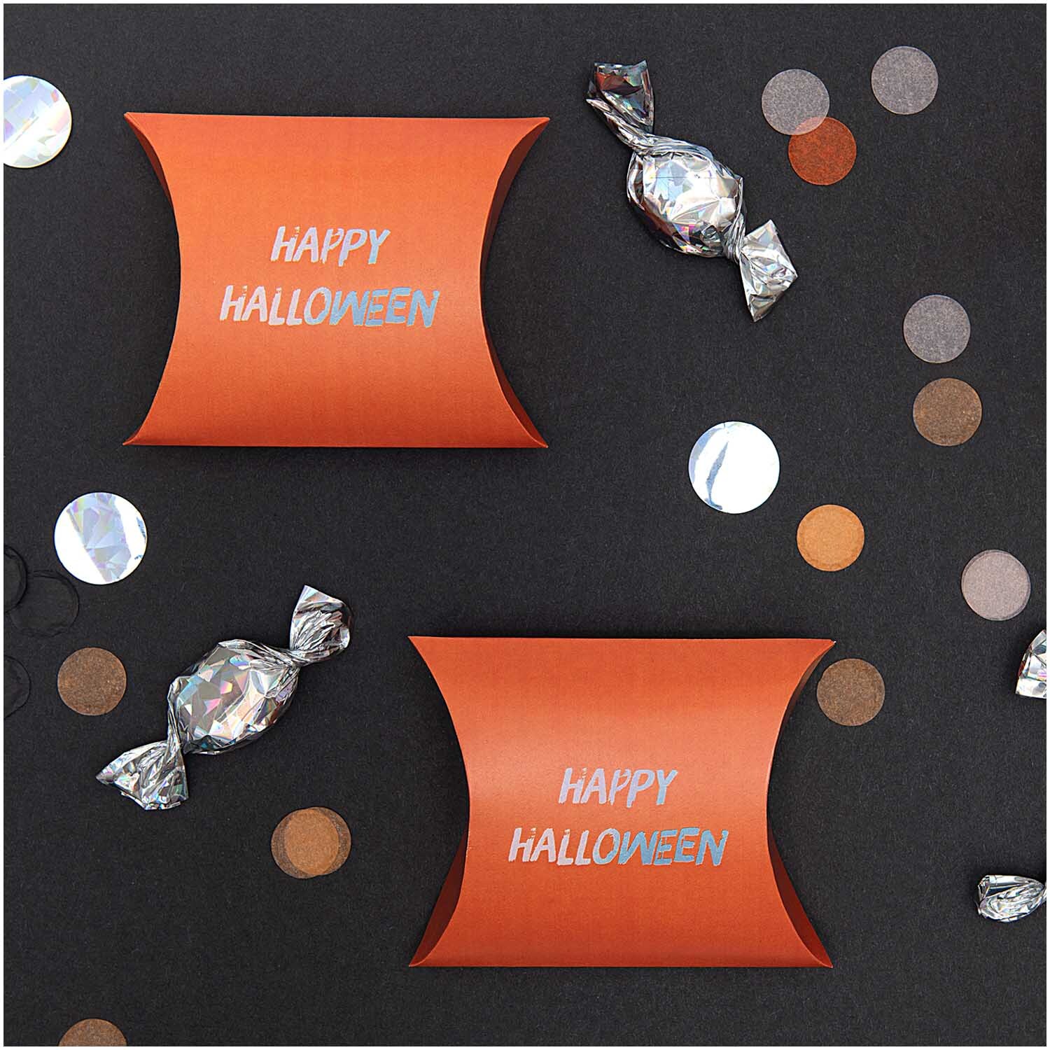 Paper Poetry Geschenkschachteln in Orange mit "Happy Halloween"-Aufdruck, umgeben von Konfetti und Bonbons.