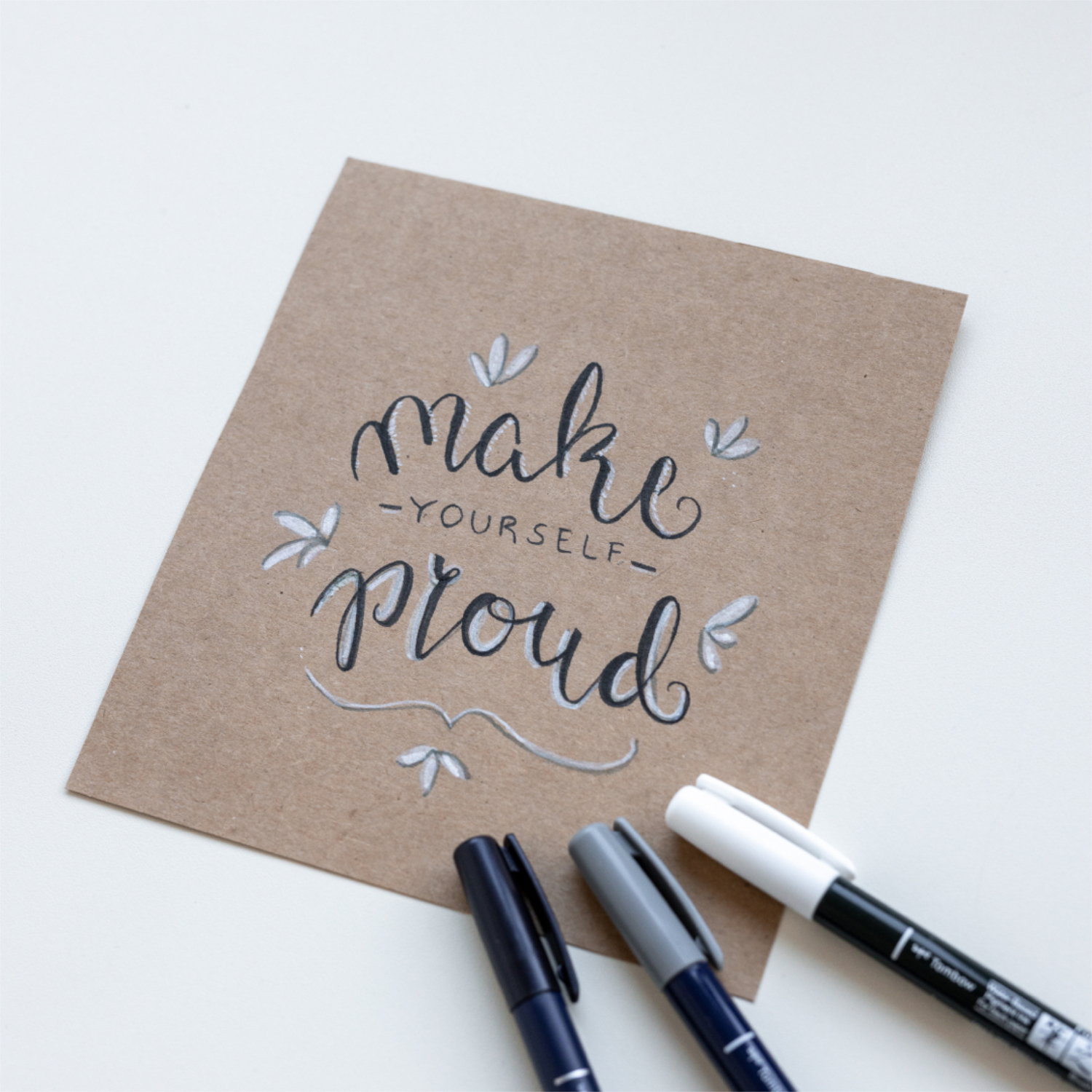 Kalligraphie Fudenosuke Nr. 1 grau: Handgeschriebener Spruch auf braunem Papier, umgeben von drei Stiften.