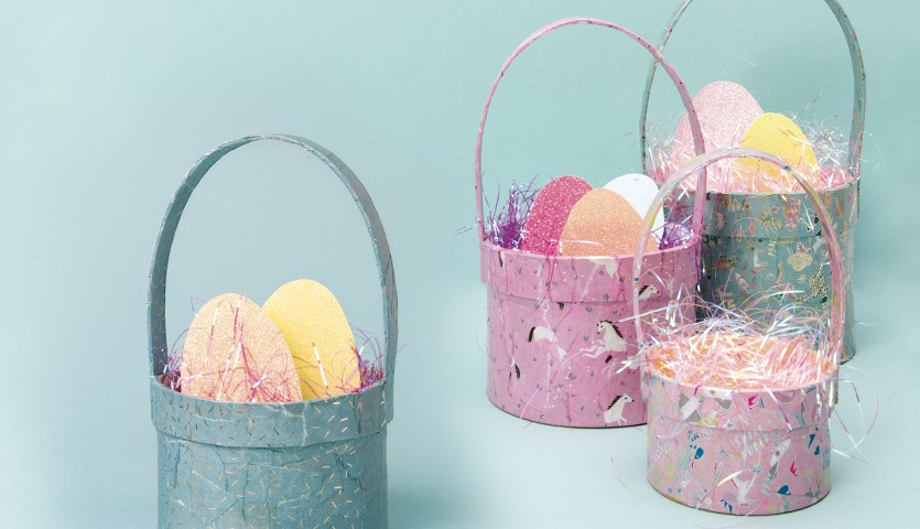 Bastelanleitung Osterkörbchen: Vier bunte Körbchen mit Ostereiern und Ostergras auf blauem Hintergrund.