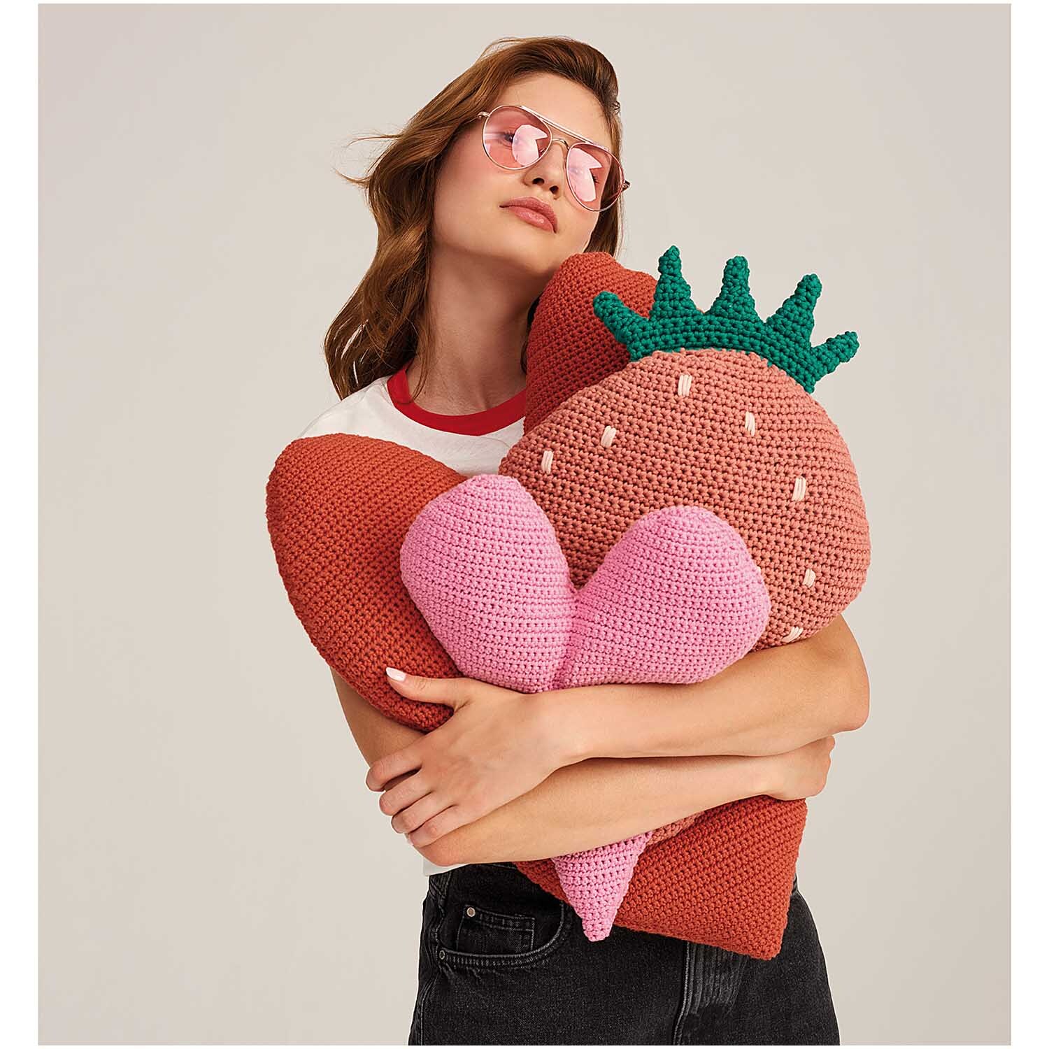 Fashion Jersey: Frau umarmt gestricktes Kissen in Erdbeerform, trägt Sonnenbrille und T-Shirt.