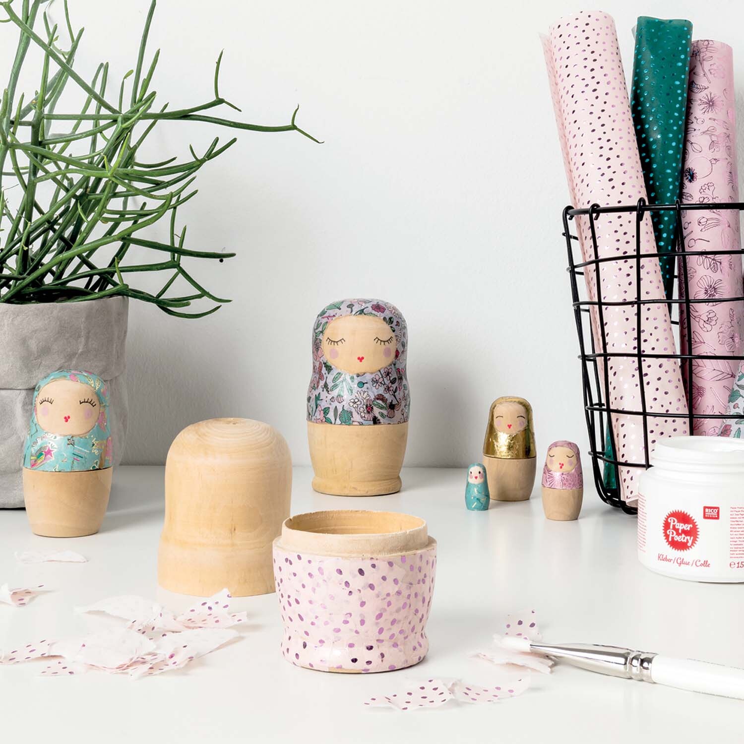 Bastelanleitung bunte Matroschkas: Handbemalte Holzpuppen auf einem Tisch mit Bastelmaterialien und Pflanzen.
