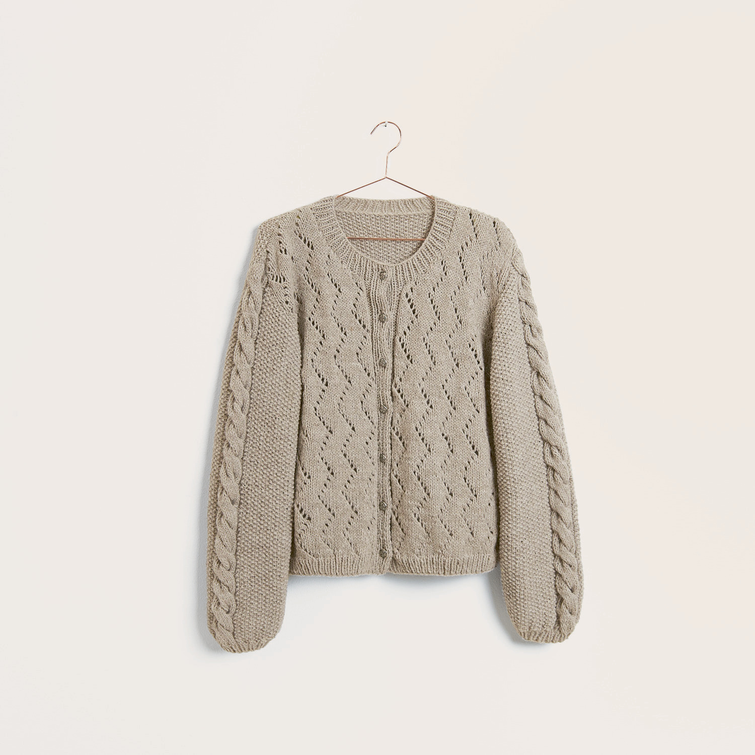 Strickset Jacke Modell 01c aus Trachtenbuch I mog di, beige, mit Trachtenknöpfen und Webmuster von Rico Design, hängt an einem Kleiderbügel.