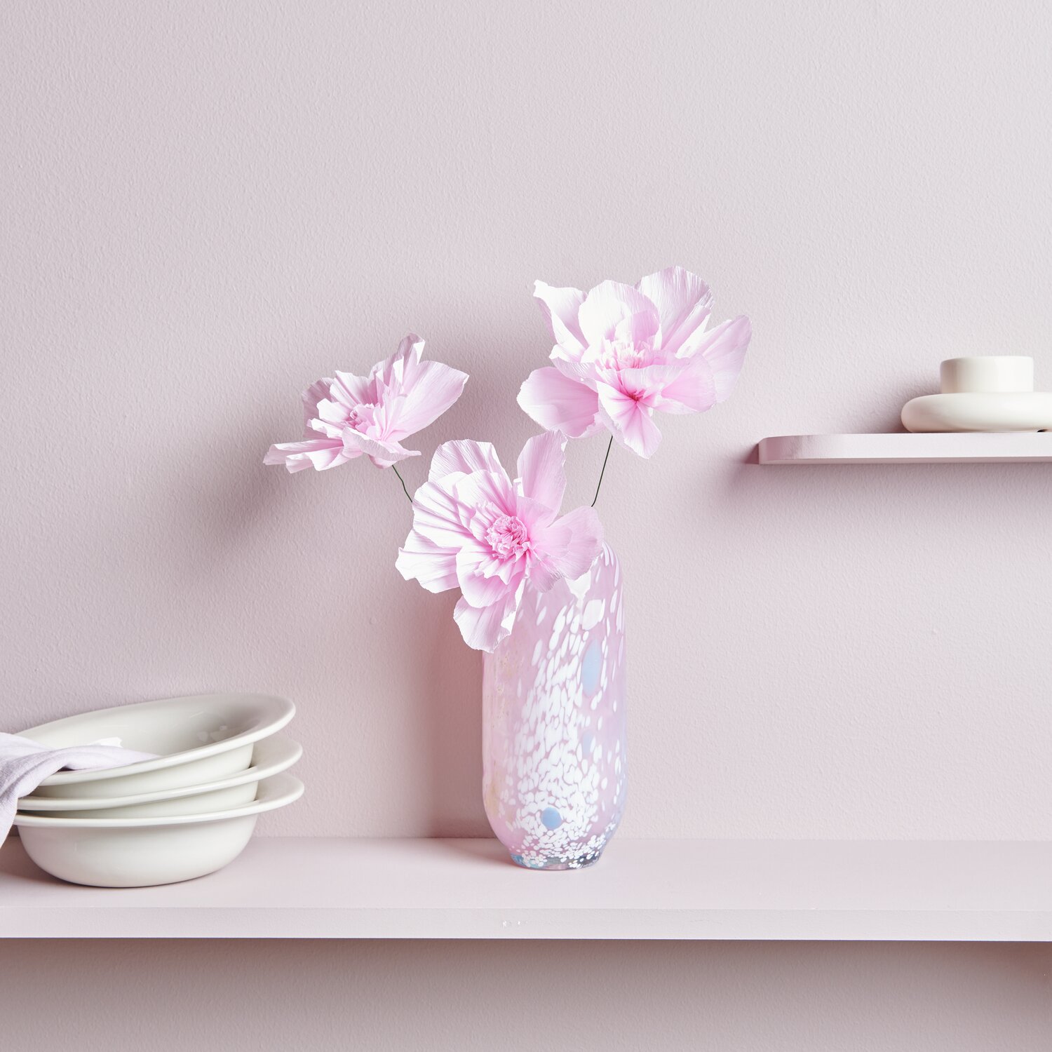 Krepppapier Blüten in zartem Rosa von Rico Design, arrangiert in einer eleganten Vase auf einem Regal.