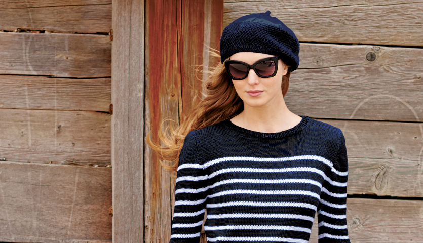 Strickanleitung Pullover und Baskenmütze im Navy-Look: Frau in gestreiftem Pullover und Baskenmütze vor Holzwand.