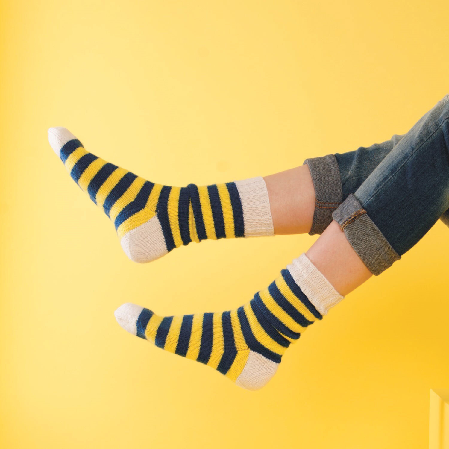 Füße tragen gestrickte Ringelsocken aus gelbem, blauem und weißem Garn.