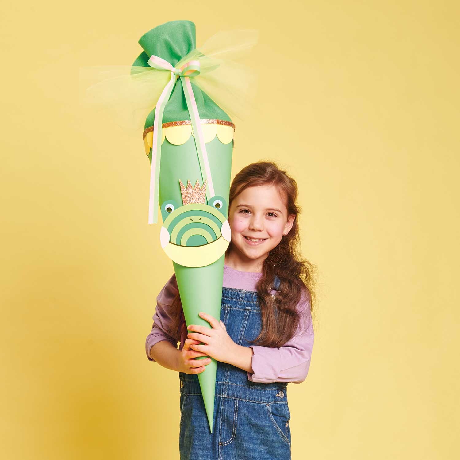 Bastelanleitung Schultüte Frosch: Ein Mädchen hält eine grüne Schultüte mit Froschmotiv und Krone.