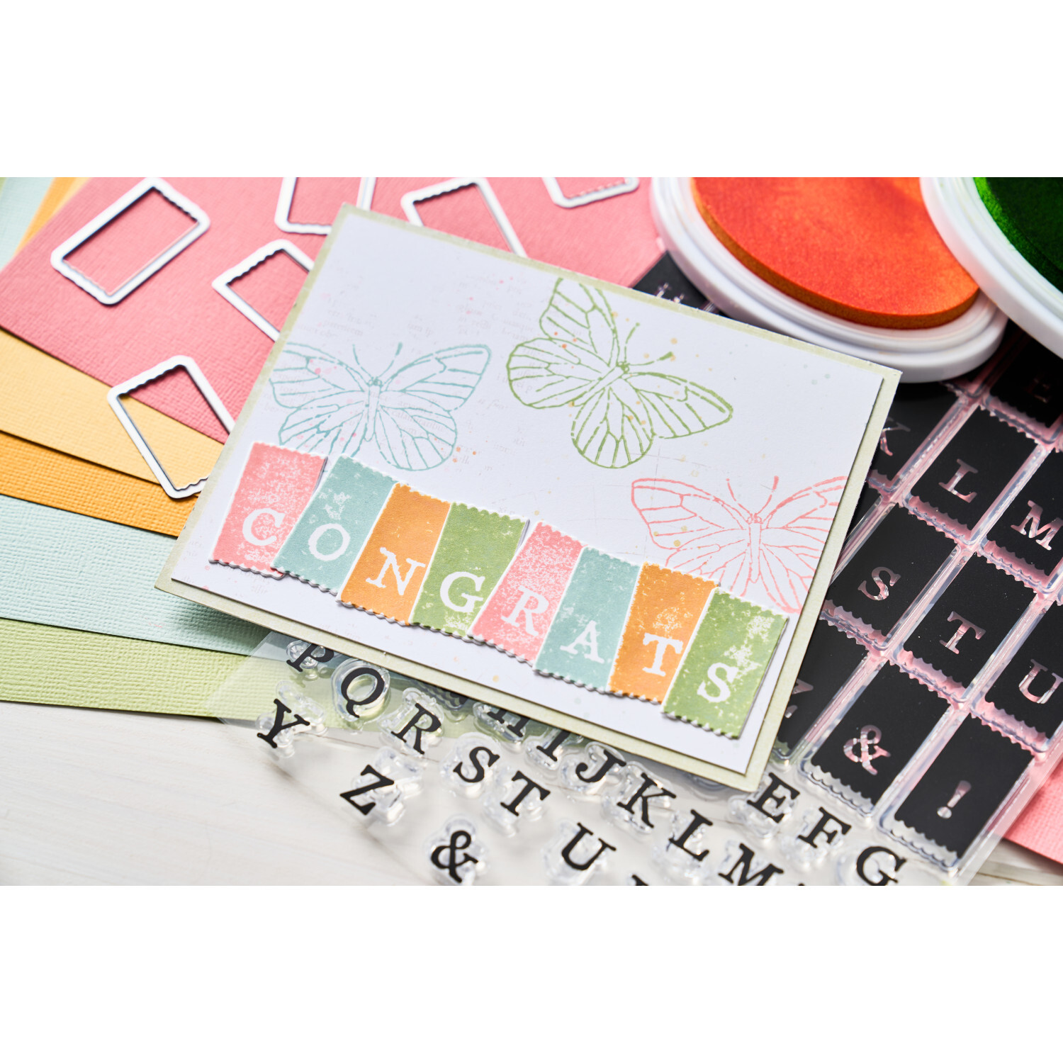 Painted Pencil Butterflies Clear Stamps Set auf bunter Karte mit Schmetterlingsmotiv und "Congrats"-Schriftzug, umgeben von Stempelkissen und Buchstaben.