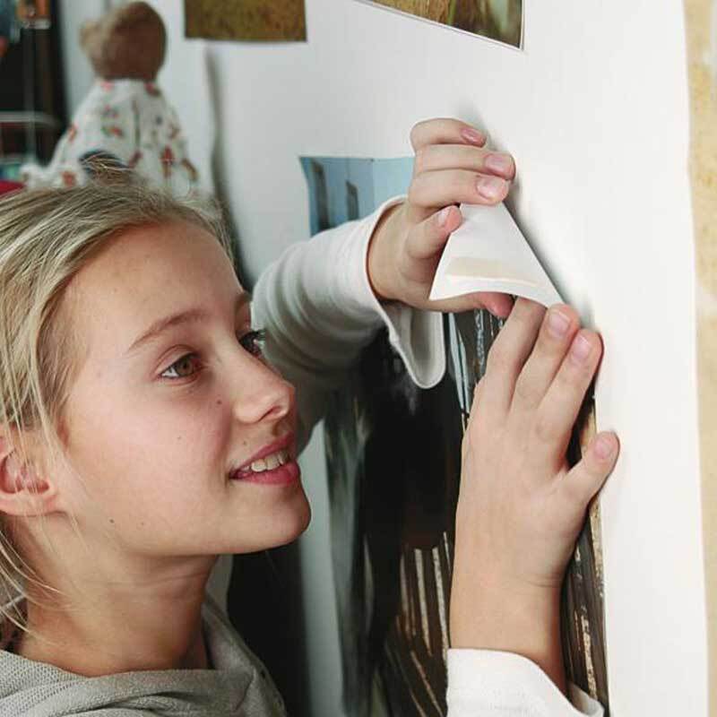 Powerstrips Poster 20 Stück: Ein Kind befestigt ein Poster mit einem weißen Klebestreifen an der Wand. Ideal für einfache und saubere Dekoration.