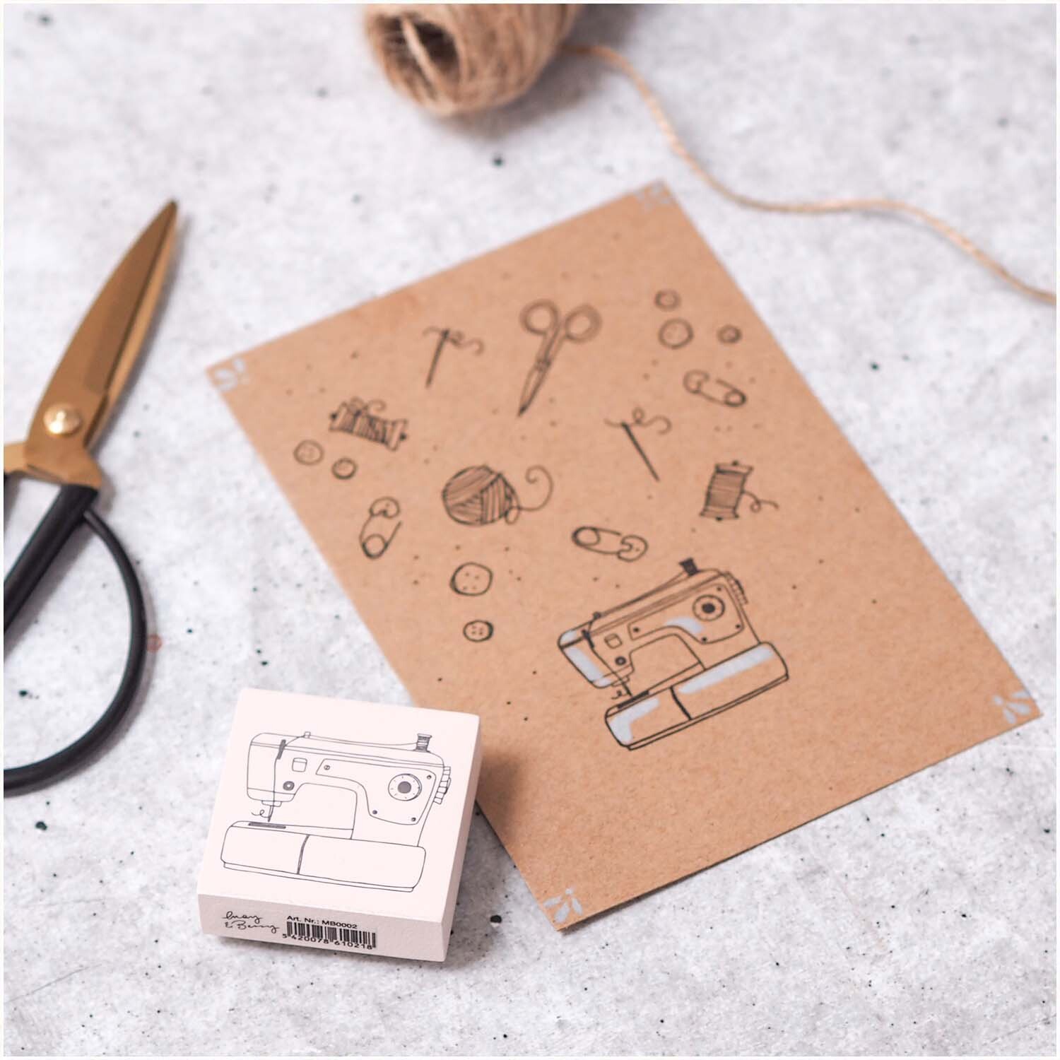 Stempel Nähmaschine 45x45mm von May&Berry in Rosa, abgebildet neben einer Karte mit Nähmotiven und einer Schere.