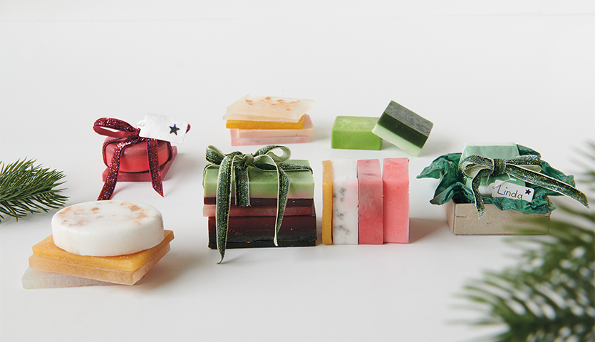 Anleitung Seife gießen und weihnachtlich verpacken: Verschiedene bunte Seifenstücke, festlich dekoriert mit Schleifen und Tannenzweigen.