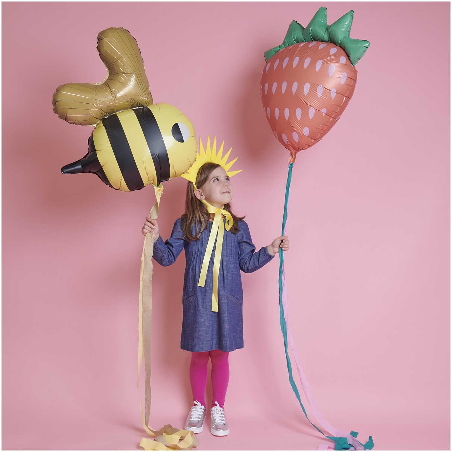 Haarreif Sonne 34x26cm: Kind mit gelbem Haarreif von Rico Design, hält Bienen- und Erdbeerballon.