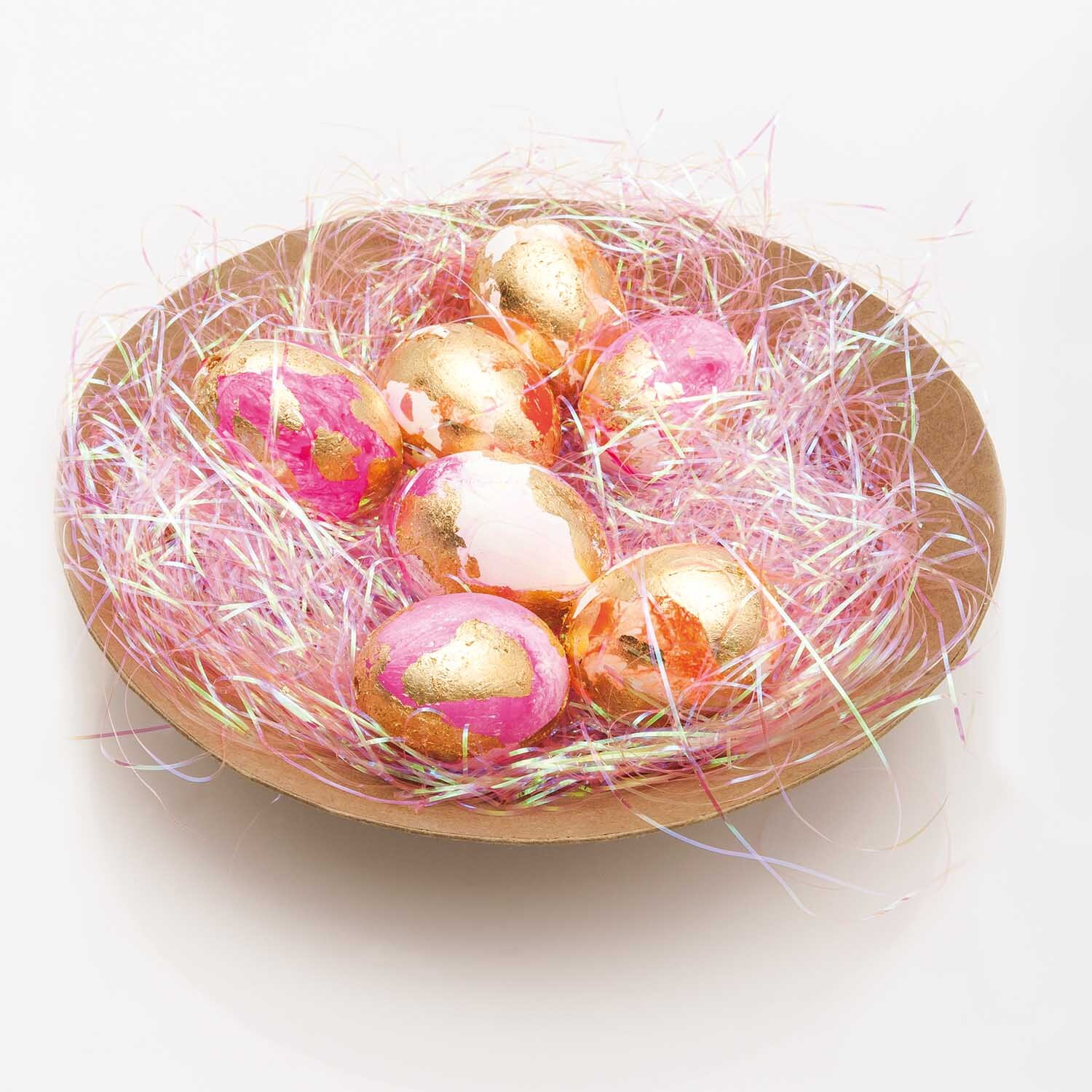 Bastelanleitung Ostereier mit Blattmetall: Goldene und rosa Ostereier in einem Nest aus buntem Stroh.