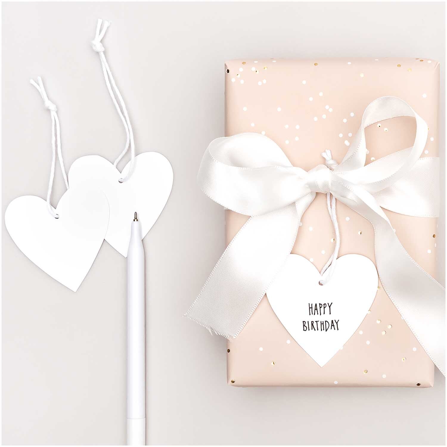 Paper Poetry Papieranhänger Herzen M 24 Stück: Weiße Herzanhänger neben Geschenk mit Schleife. Ideal für kreative Dekorationen.