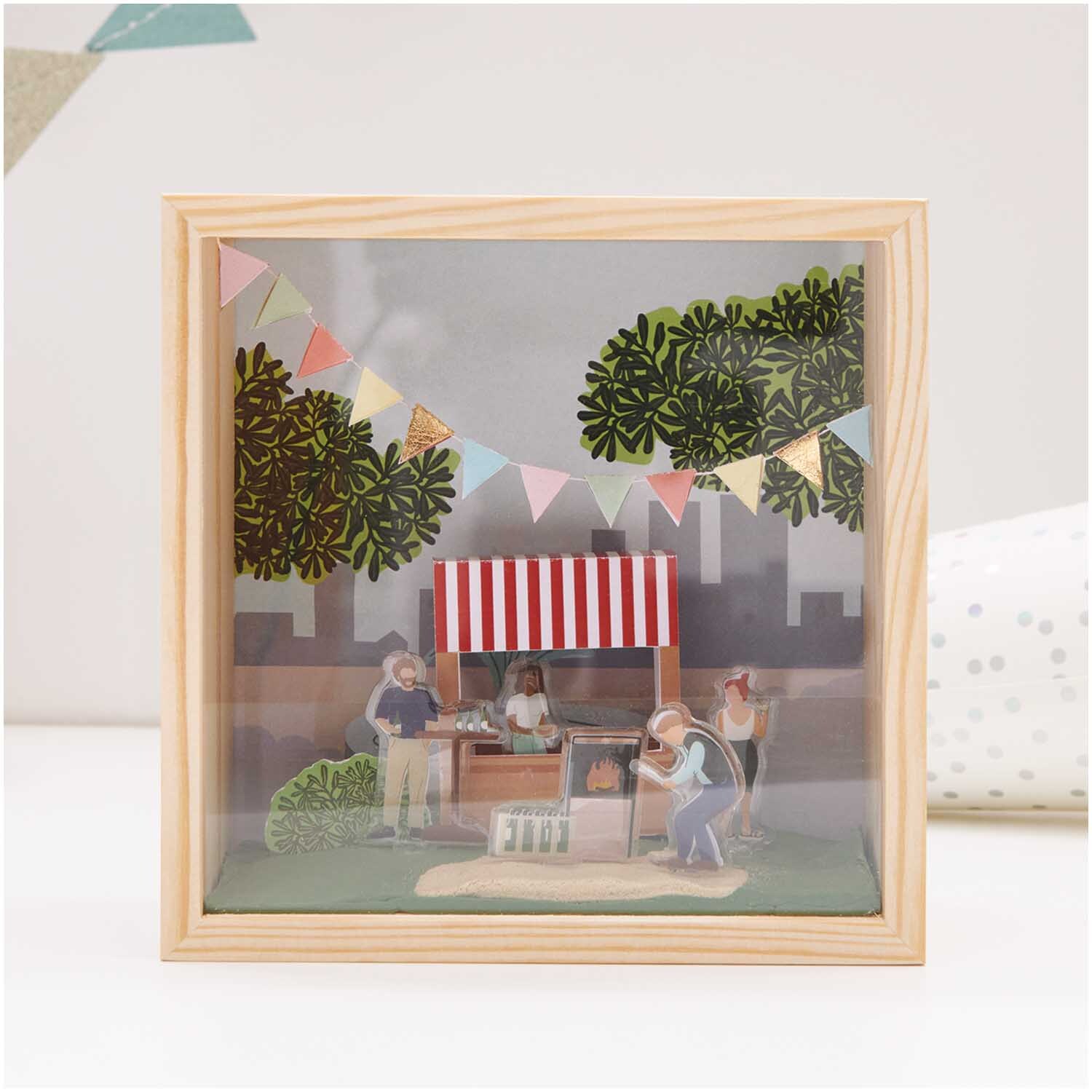Figurico Modelliermasse 28g: Szene mit Marktstand, Menschen und Bäumen in einem Holzrahmen, verziert mit Wimpeln.