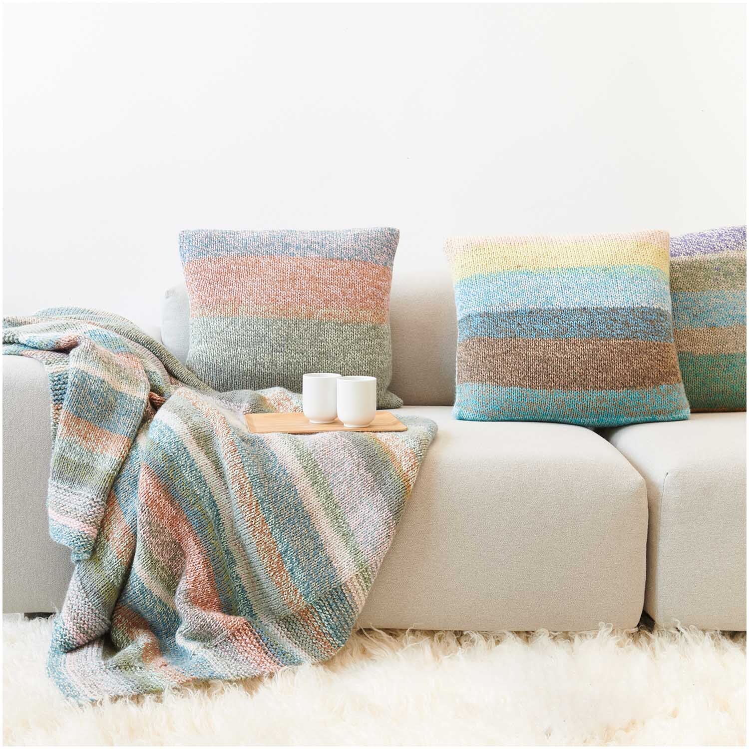 Strickset Kissen Modell 04 aus Die Neue Masche Nr. 7: Bunte Kissen und Decke auf beigem Sofa.