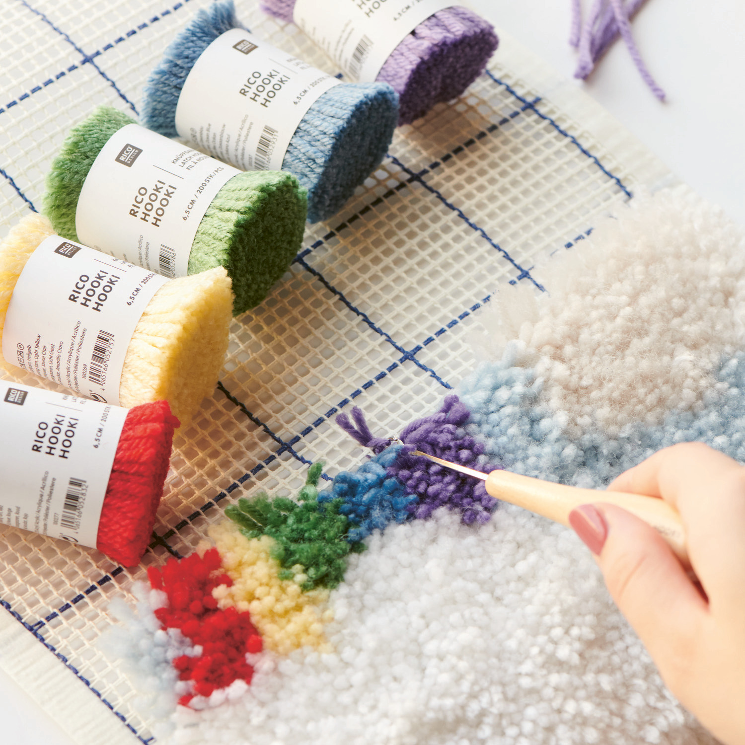 Rico Hooki Hooki Knüpfgarn in verschiedenen Farben auf einem Knüpfstramin, mit Hand beim Knüpfen.