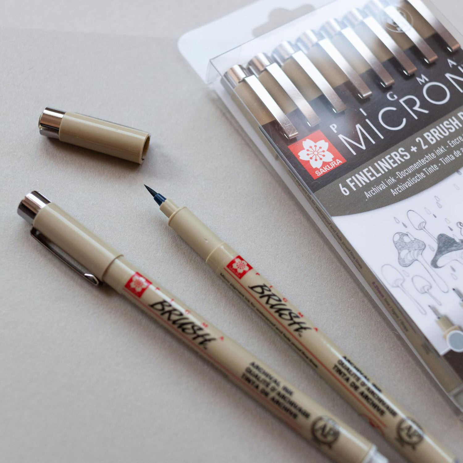 Pigment Liner Sakura Pigma Micron Fineliner Set Kaltgrau zeigt Stifte in Beige auf hellem Hintergrund.