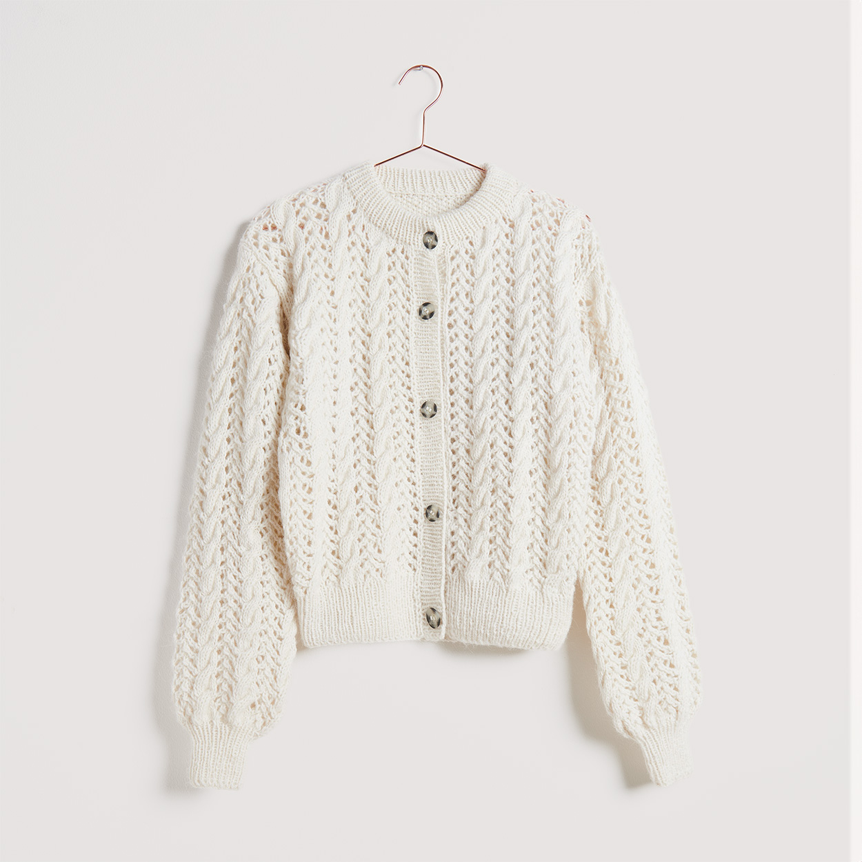 Zopf- & Lochmuster Jacke auf grauem Hintergrund – zum Strickset
