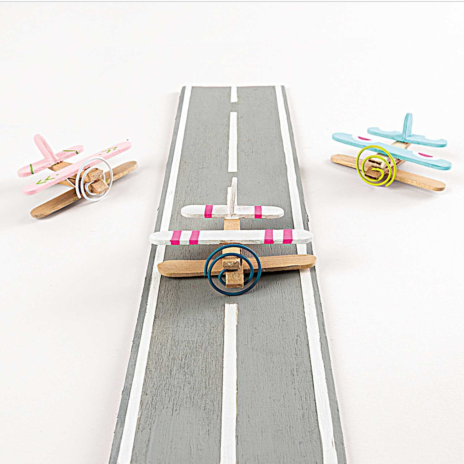 DIY-Holzbastelset: Drei bunte Holzflugzeuge auf einer grauen Startbahn, 140-teilig von Rico Design.