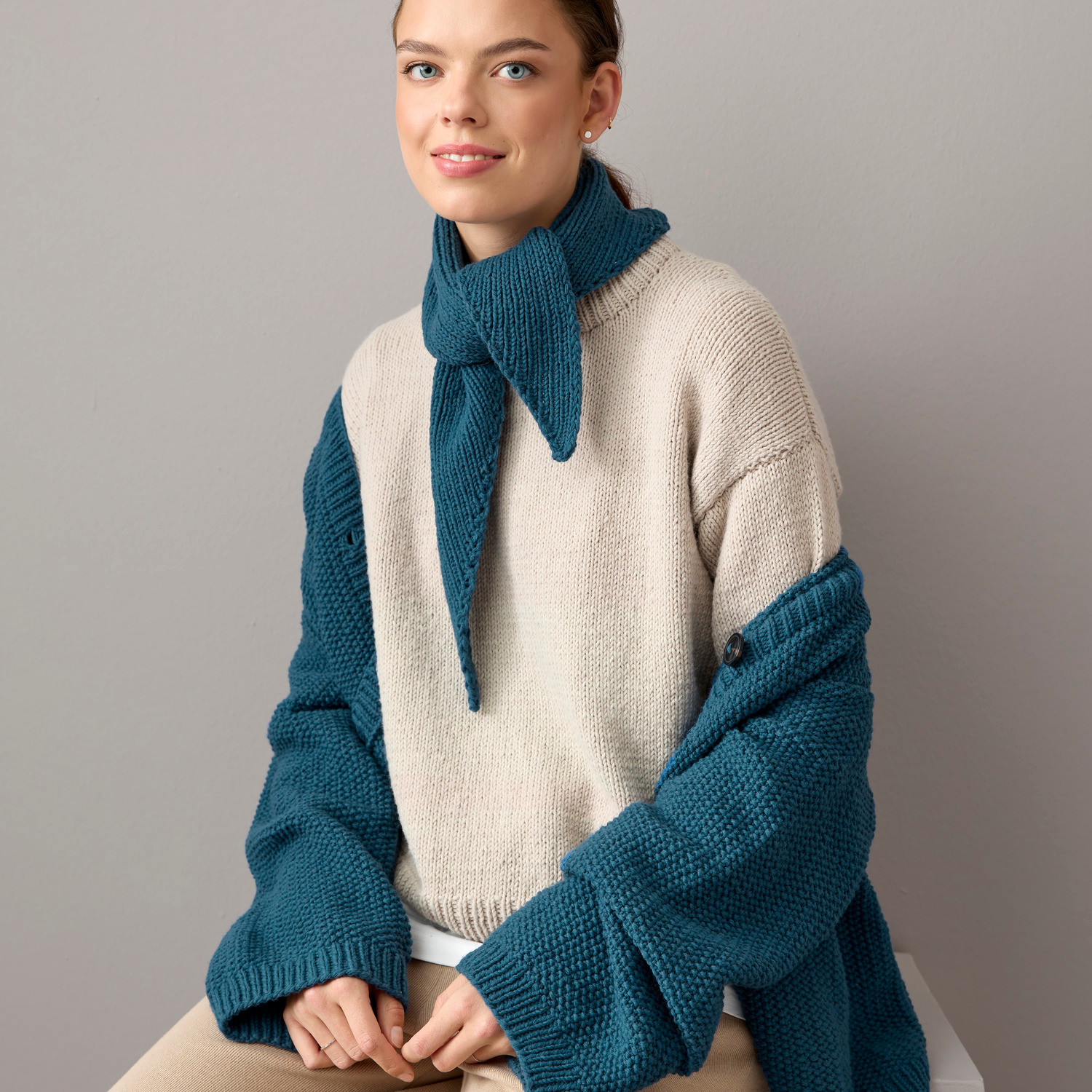 Essentials Vegan Cashmere aran: Frau trägt gestricktes Dreieckstuch in Petrol und Beige von Rico Design. Ideal für stilvolle, vegane Mode.