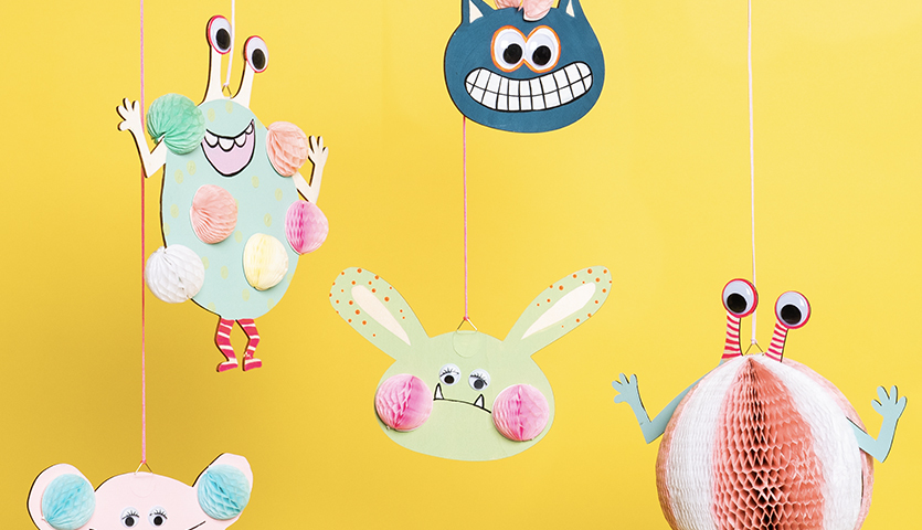 Bastelanleitung Monster-Mobilé aus Wall Charms: Bunte, hängende Monsterfiguren vor gelbem Hintergrund.