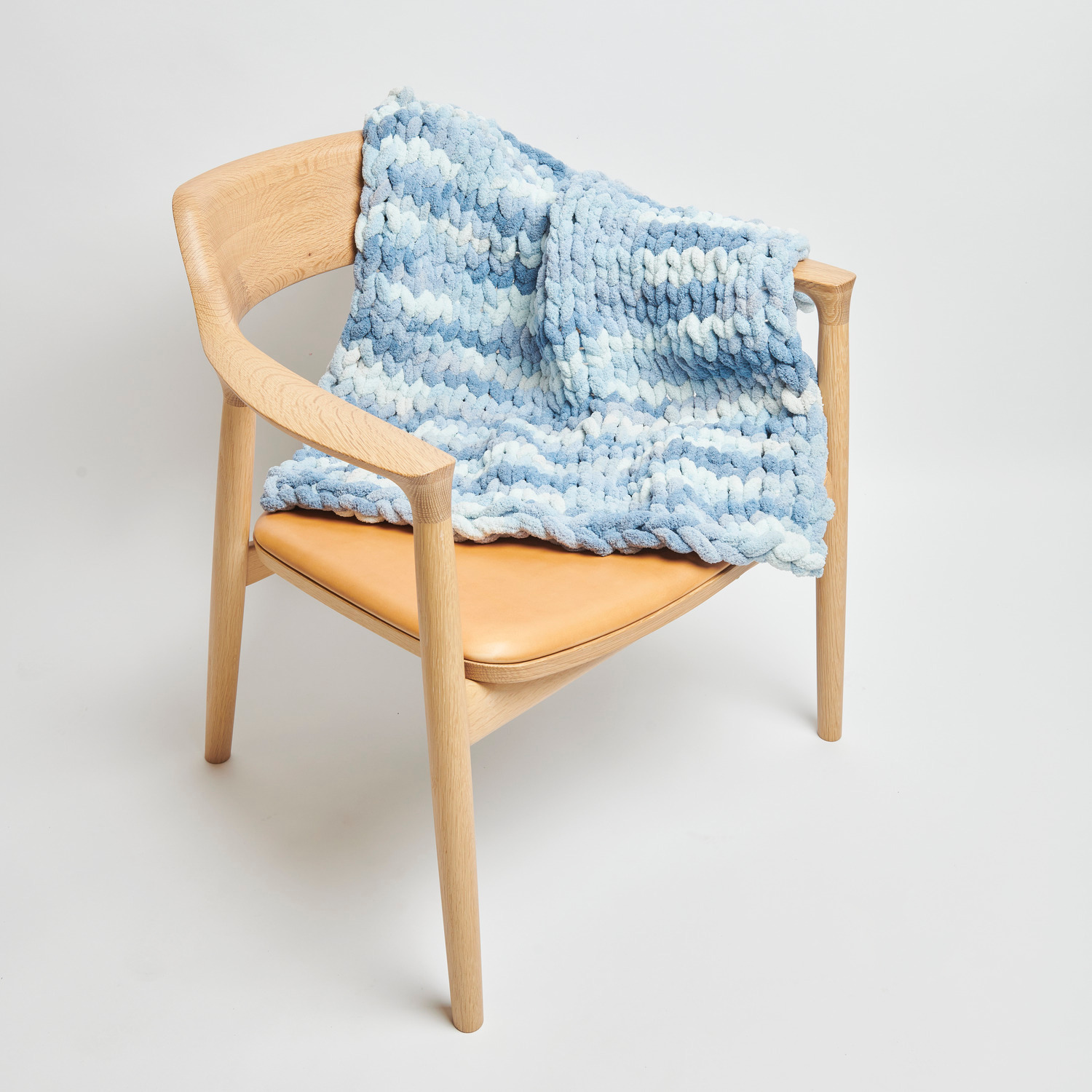 Chenillove Super Big Print: Weiche, blaue Strickdecke von Rico Design auf einem modernen Holzstuhl.