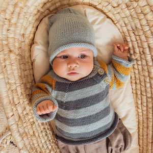 Baby liegt in Körbchen und trägt Strickmütze und Strickpullover. 
