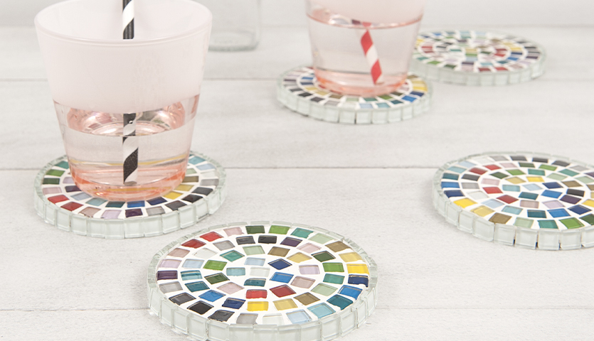 Bastelanleitung Deko mit Mosaiksteine: Bunte Mosaik-Untersetzer auf hellem Tisch mit Gläsern.