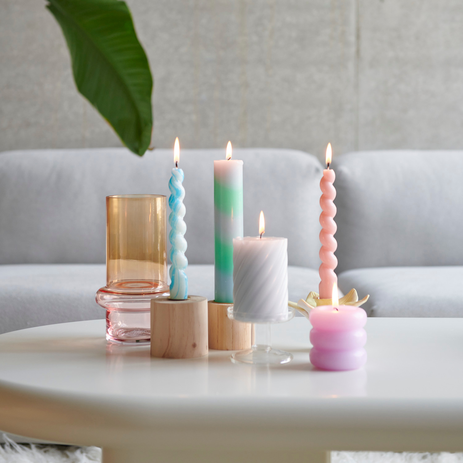 Stumpenkerze Ring auf einem runden Holz-Kerzenhalter, umgeben von weiteren Kerzen in Rosa und Mint.