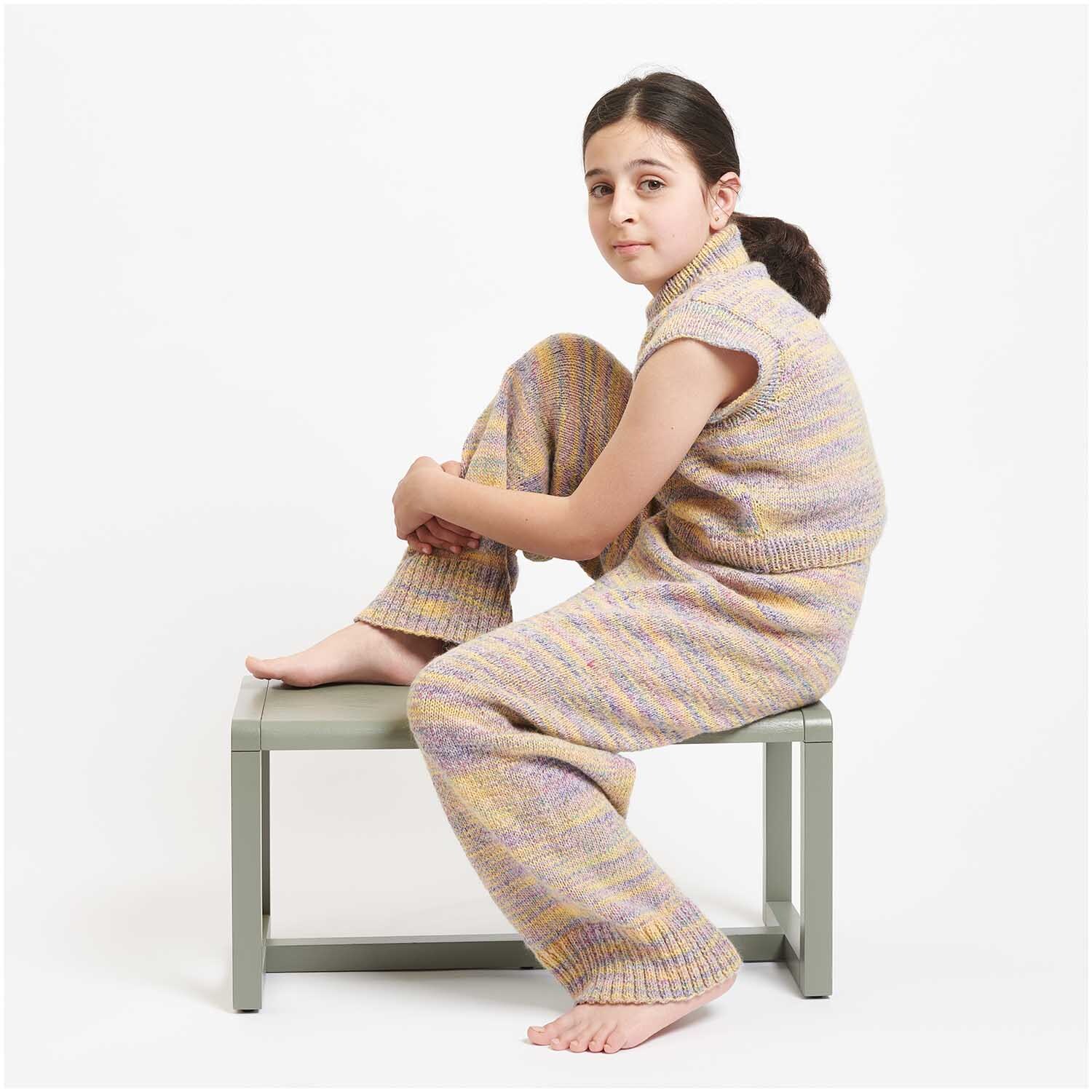 Creative Colour Shift dk: Kind in gestricktem Pastel-Outfit von Rico Design, sitzt auf einem Hocker.
