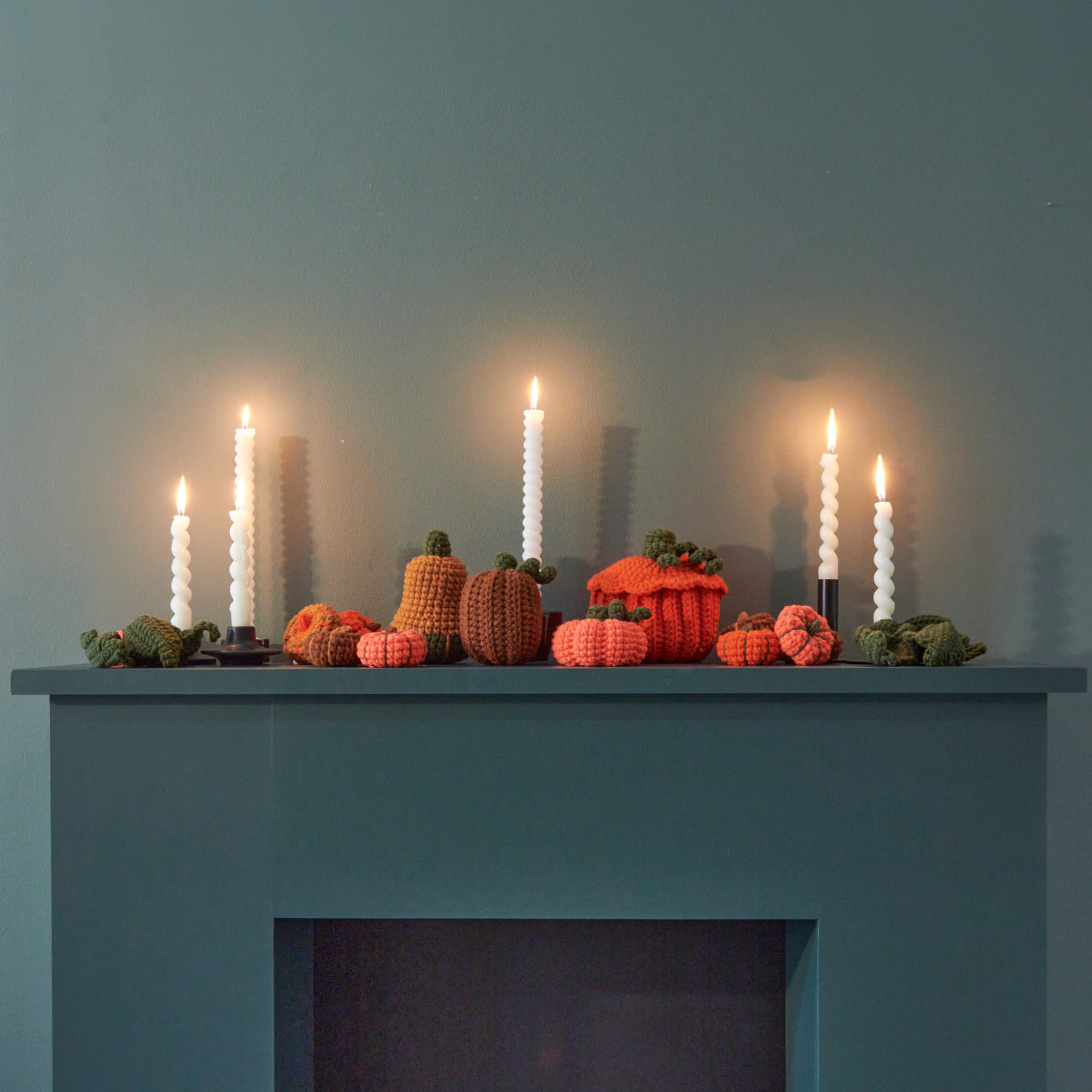 Häkelset Pumpkins: Handgefertigte Kürbisse in Orange und Grün auf einem Kamin, dekoriert mit weißen Kerzen. Perfekt für herbstliche Akzente.