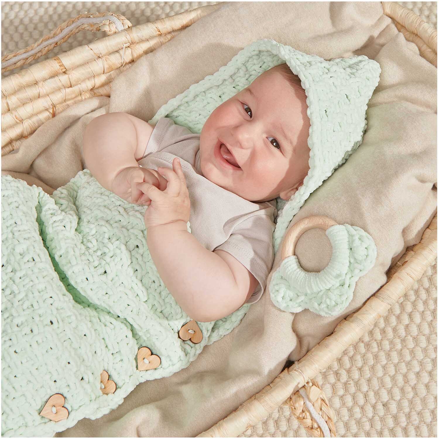 Creative Chenillove: Ein Baby liegt in einem mintfarbenen Strickset von Rico Design in einem Korb.