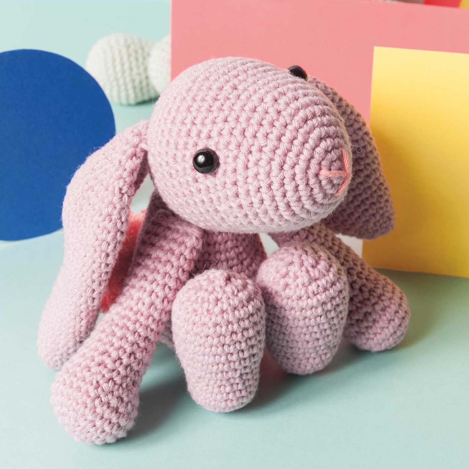 Häkelanleitung Schlappohr-Hase: Rosa gehäkelter Hase mit langen Ohren vor buntem Hintergrund. Ideal für DIY-Projekte.
