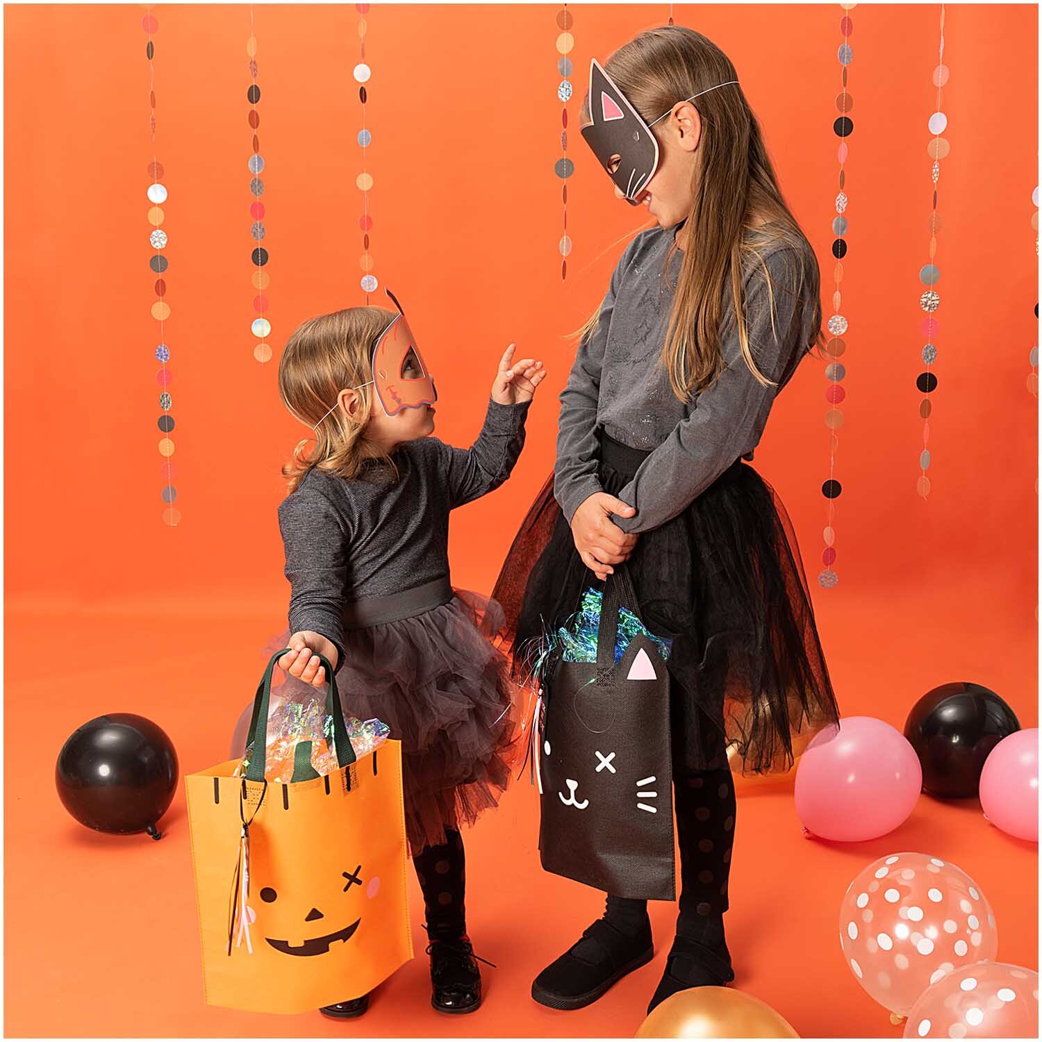 Paper Poetry Geschenktüte Kürbis 28x30cm: Zwei Kinder in Halloween-Kostümen mit Geschenktüten vor orangefarbenem Hintergrund.