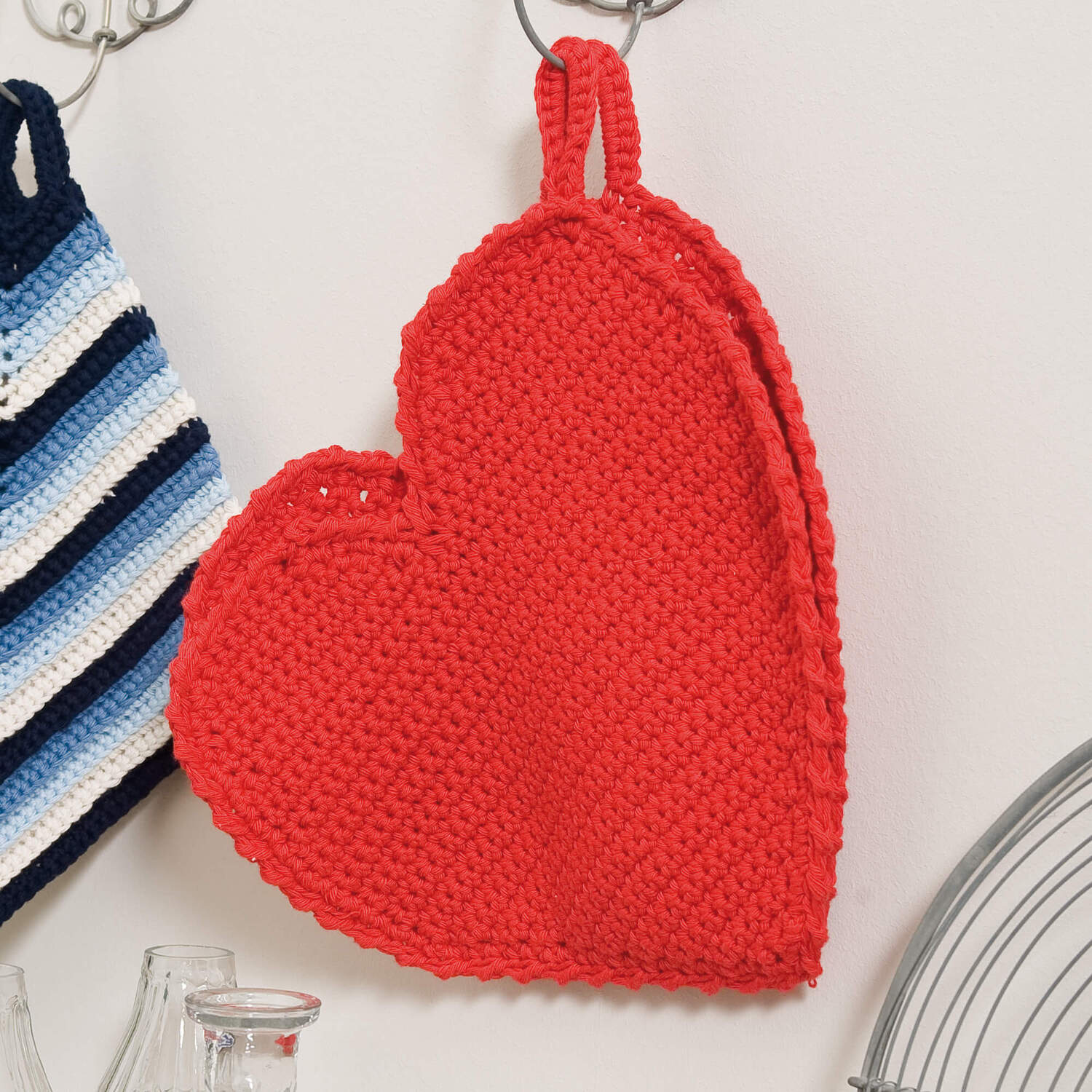Häkelanleitung Herztopflappen aus rotem Garn, dekorativ an der Wand hängend. Ideal für Küche.