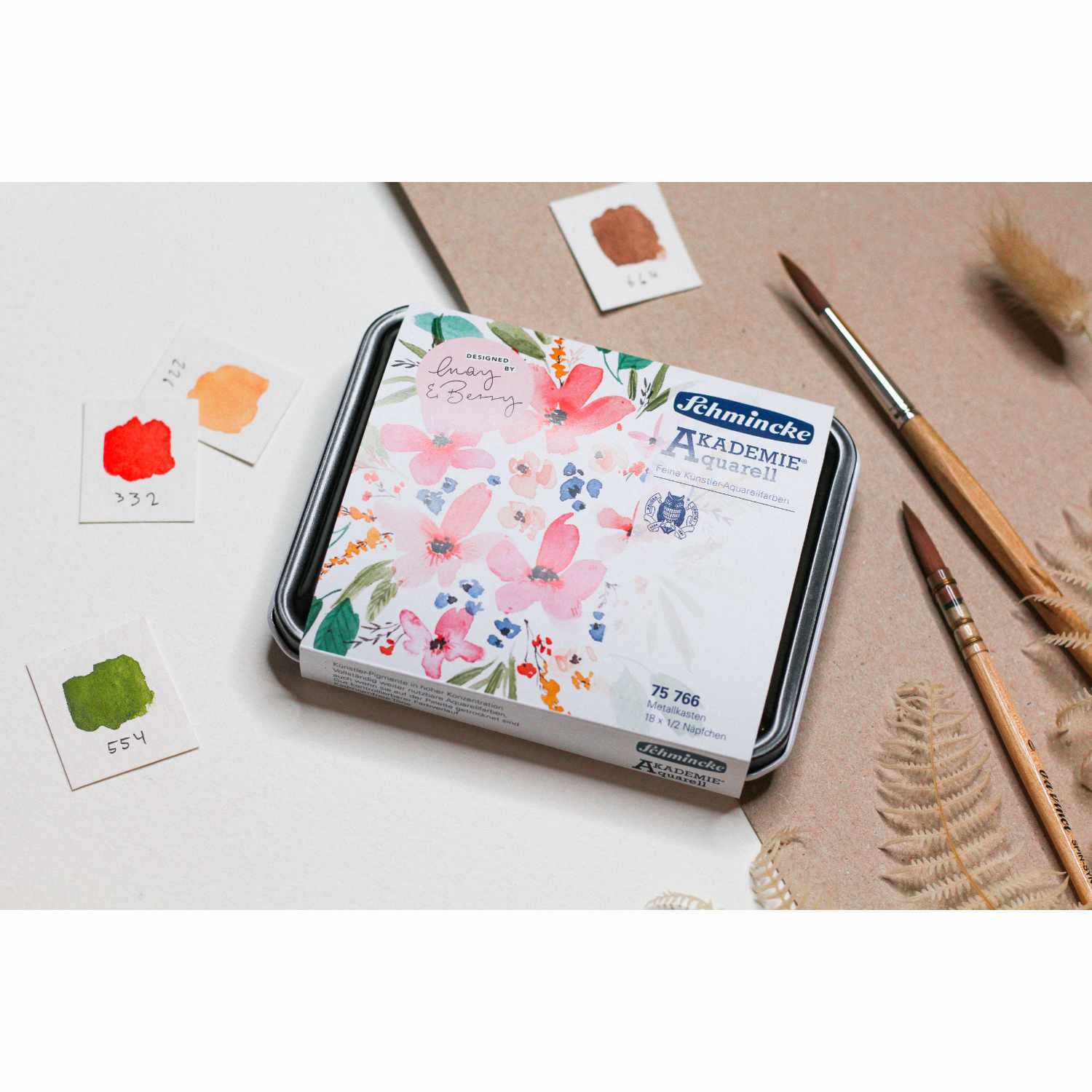 Schmincke Akademie Aquarellkasten mit 18 Farben, umgeben von Pinseln und Farbmusterkarten.
