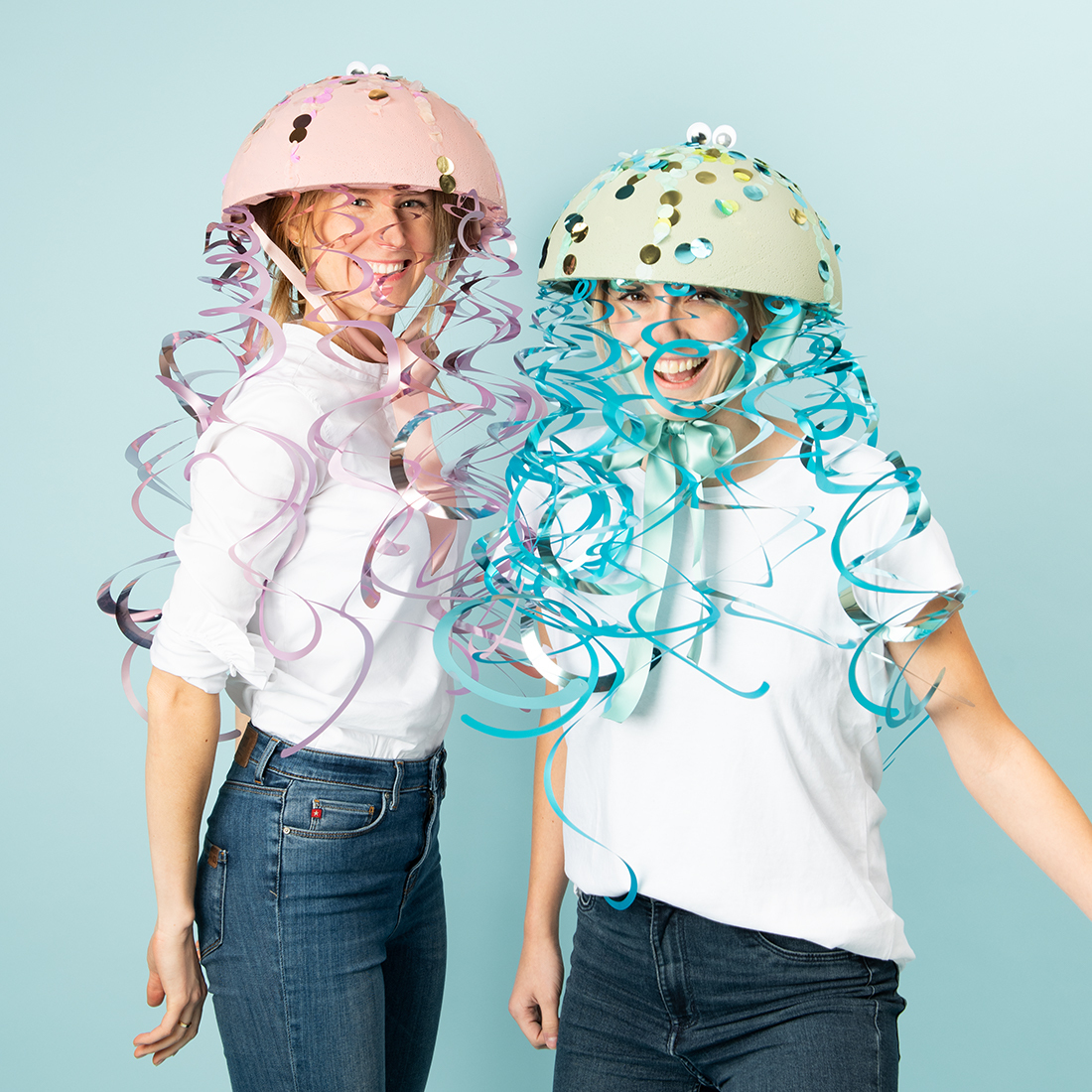 Bastelanleitung bunten Quallen-Kopfschmuck: Zwei Personen tragen kreative Helme mit bunten Bändern und Pailletten.