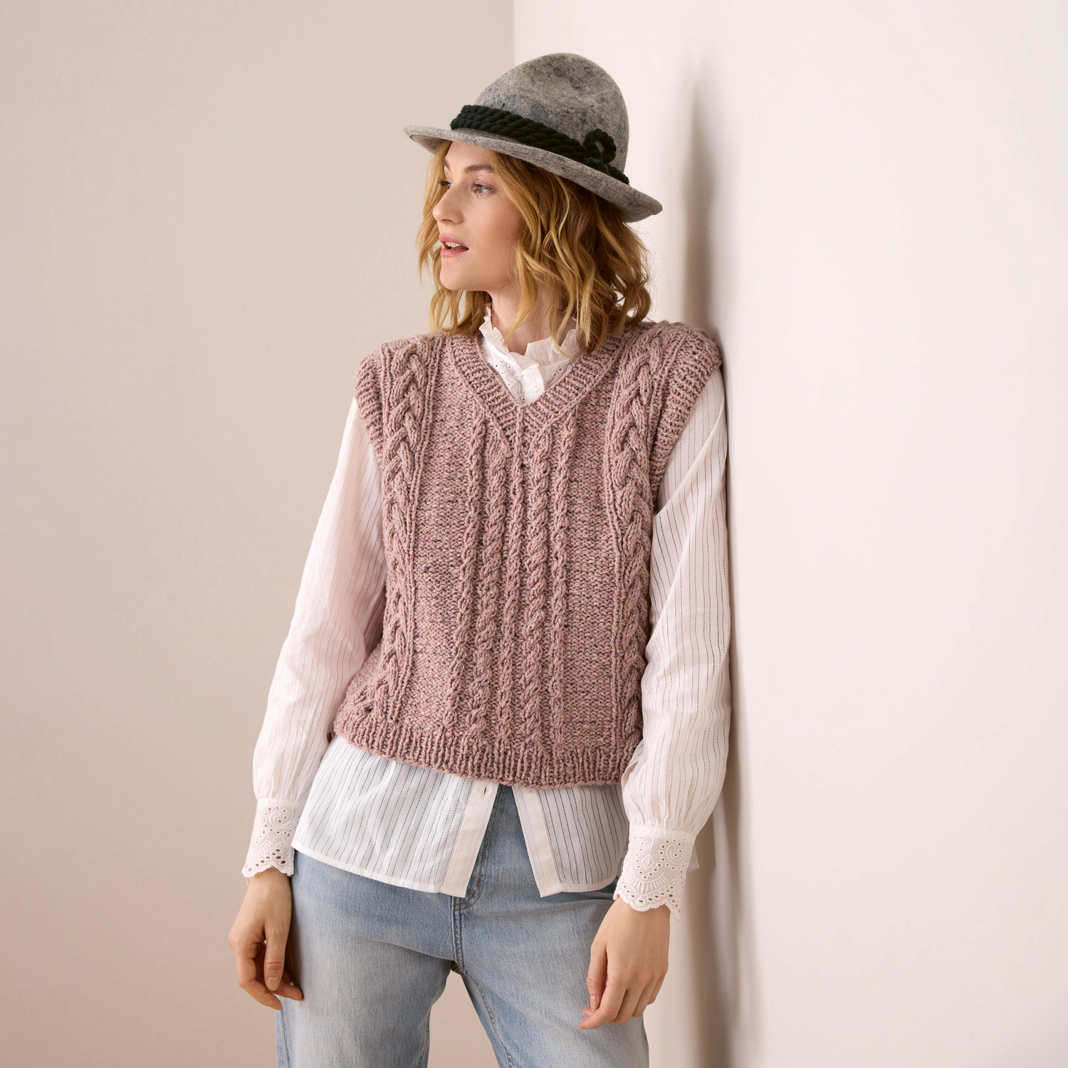 Strickset Damenpullunder Modell 21 aus Trachtenbuch I mog di: Frau trägt rosa Pullunder über weißer Bluse, kombiniert mit grauem Hut und Jeans.